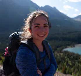 devin wearing a backpack in front of mountains and a river